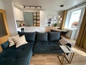 a living room with a black couch and a kitchen at Alėjos Apartmentai Comfort in Druskininkai