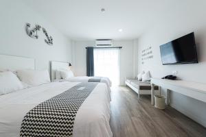 a white bedroom with two beds and a flat screen tv at Peggy's Cove Resort in Chao Lao Beach