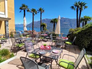 eine Terrasse mit Tischen, Stühlen und Palmen in der Unterkunft Garden Hotel Primavera in Brissago