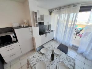 uma cozinha com armários brancos e uma mesa e cadeiras em Appartement Village Naturiste Paradoxe em Cap d'Agde