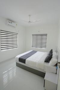 a white bedroom with a bed and two windows at Yelza Hotel and Residence in Alwaye