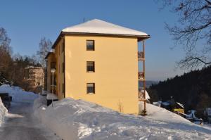 un bâtiment jaune avec un tas de neige autour de lui dans l'établissement Apartman Kamila, à Janské Lázně