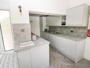 a white kitchen with white cabinets and a sink at 2 Salt Cottage in Swansea