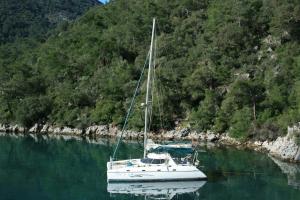 a white boat in the water next to a mountain at On Y Va , Delightful 3 bedroom catarmaran, with skipper in Marmaris