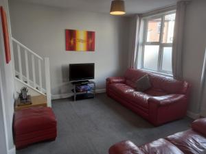 a living room with a red leather couch and a television at Springfield Gardens - 4 Bedroom House, 8 Beds, Close to J26 M1-A52 - Ilkeston - Long Eaton - Nottingham - Derbyshire - 400Mbs WiFi Free Parking! in Ilkeston