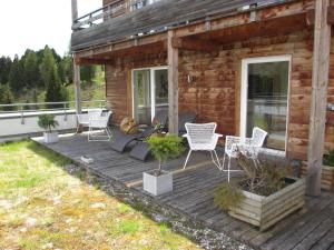 eine Holzterrasse mit weißen Stühlen und ein Haus in der Unterkunft Zirbensuite Turracher Höhe in Turracher Hohe