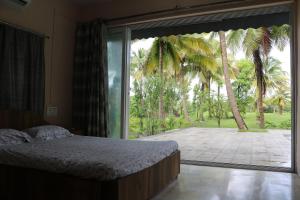 um quarto com uma cama e uma grande janela de vidro em Priti Garden Farmstay, Kelva Palghar em Māhīm