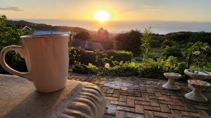 una taza de café sentada en una cornisa de piedra con la puesta de sol en Seaview Villa 25, en Shelly Beach