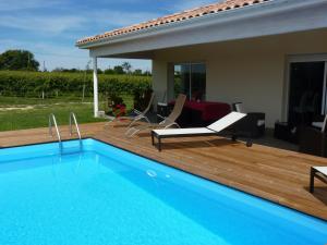 una piscina en una terraza de madera con sillas y una casa en Gîte Les Vignes en Cravencères