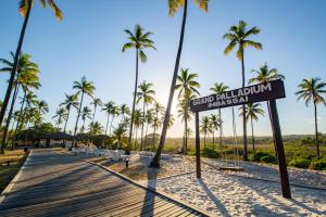 a sign on a boardwalk on a beach with palm trees at Grand Palladium Imbassaí Resort & Spa - All Inclusive in Imbassai