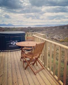 a wooden table and chair on a deck with a trash can at Duirinish Pods with Private Hot Tubs and Duirinish Bothy with No Hot Tub in Plockton
