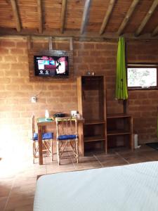 a room with a table and a tv on a brick wall at Chalés Portal Verde - Seja bem vindo in Carrancas