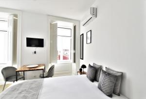 a white bedroom with a bed and a desk and window at Sophia Studios in Coimbra