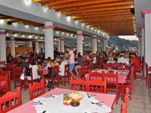a group of people sitting at tables in a restaurant at Pink Palace Beach Resort in Agios Gordios