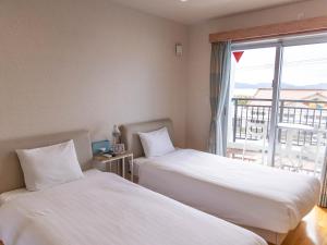 two beds in a hotel room with a window at YANBARU STAY ちゅら宿 in Nago