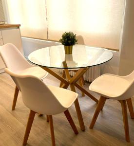 une table en verre avec quatre chaises blanches et une plante en pot dans l'établissement Apartamentos Aranda - VUT- La Cepa I - II, à Aranda de Duero