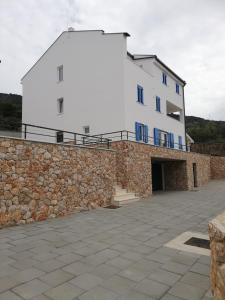 a large white building with blue windows and a stone wall at FRANTA in Cres