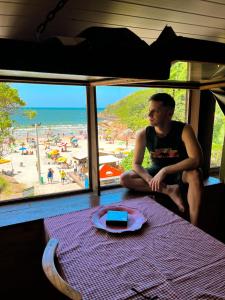 un hombre sentado en una mesa mirando a una playa en Mona lisa, en Florianópolis