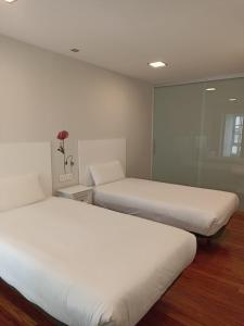 two beds in a room with white walls and wood floors at Campanas Haus in Santiago de Compostela