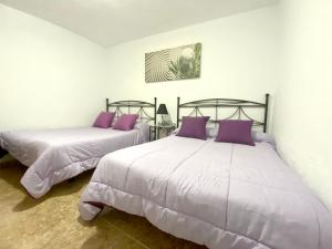 - 2 lits dans une chambre blanche avec des oreillers violets dans l'établissement 4 bedrooms house with enclosed garden and wifi at Ingenio, à Ingenio
