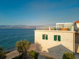a building with green shuttered windows next to the water at SEAFRONT NORTH HOUSE SUTIVAN - new luxury three-bedroom villa - unforgettable panoramic views of the sea - roof terrace with jacuzzi - first row next to the beach and right next to all facilities - secured parking in Sutivan