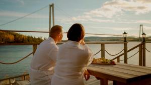 a man and a woman sitting at a picnic table overlooking the water at Björkuddens Hotell & Restaurang in Sandöverken