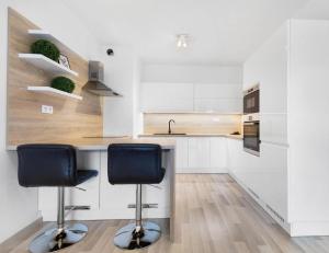 a white kitchen with two chairs at a counter at Sunflower - Modern large charming apartment with balcony in Bratislava