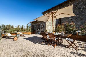a patio with a table and chairs and an umbrella at Appartamento in casale con piscina Casa I Pavoni in Chianni