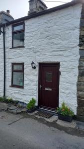 a white house with a brown door and two windows at Merrion Cottage Penmachno Betws y Coed Conwy in Penmachno