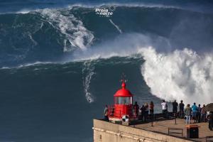a red lighthouse on a pier with a large wave at Alojamento Rosa in Nazaré