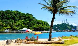 Dos personas sentadas bajo una sombrilla en una playa en Casa com piscina , churrasqueira, Wi-Fi, em rua de Areia à 1km da praia, bairro sussegado, proíbido uso de som extremamente alto ideal para descansar, en Itanhaém