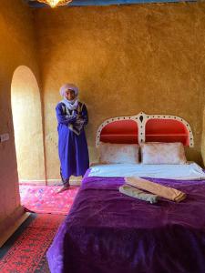 une femme debout à côté d'un lit dans une pièce dans l'établissement Dar Yaya, à M'Hamid El Ghizlane