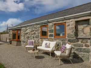 a stone cottage with chairs and a stone wall at Beudy in Chwilog