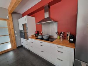 a kitchen with white cabinets and a red wall at Villa avec Piscine Les Planches à Saint Valery Somme in Saint-Valéry-sur-Somme