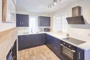 cocina con armarios azules, fregadero y fogones en Host & Stay - Gardeners Cottage, en Brafferton