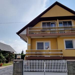 a yellow house with a white fence in front of it at Boglári Harmónia Apartman in Balatonboglár