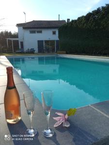 una botella de vino y dos copas junto a la piscina en Mas des Vignes Piscine chauffée, en Le Champ-Saint-Père