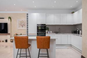 a kitchen with white cabinets and two bar stools at GuestReady - Extravagant 2BR Apt in London in London