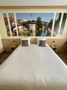 een groot wit bed met uitzicht op een brug bij Brit Hotel Montargis in Mormant-sur-Vernisson
