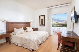 a bedroom with a bed and a desk and a window at HC Hotel Magec in Puerto de la Cruz