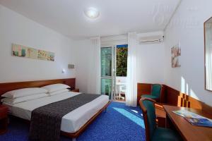 um quarto com uma cama, uma secretária e uma janela em Hotel Olympia em Lignano Sabbiadoro