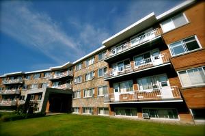 a large brick building with balconies and a yard at Beausejour Hotel Apartments/Hotel Dorval in Dorval