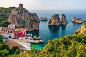 a red house in the water next to a group of rocks at La casa nel Borgo in Scopello