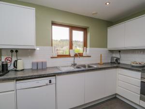 cocina con armarios blancos, fregadero y ventana en Braeside, en Coniston