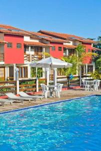 ein Swimmingpool mit Stühlen und Sonnenschirmen neben einem Gebäude in der Unterkunft Duplex Aconchegante Residencial Mont Sinai in Porto Seguro