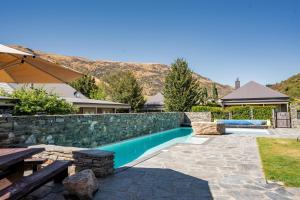 a swimming pool with a stone retaining wall and a bench at Cardrona Cottage - Cardrona Holiday Home in Cardrona
