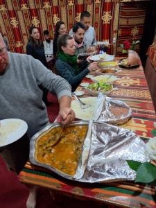 un grupo de personas sentadas alrededor de una mesa comiendo comida en Wadi rum secrets camp, en Wadi Rum