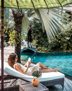a woman sitting in a chair reading a book by a pool at Blue Karma Dijiwa Seminyak in Seminyak