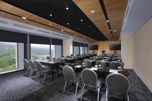 Grand ASTON Puncak Hotel & Resort في بونشاك: قاعة اجتماعات مع طاولات وكراسي ونوافذ كبيرة