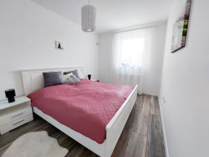 a white bedroom with a bed with a red blanket at Juhar Apartman in Kőszeg